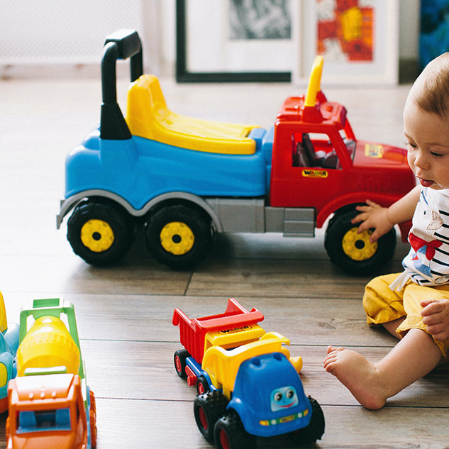Baby playing on the ground with brightly colored plastic trucks big and small