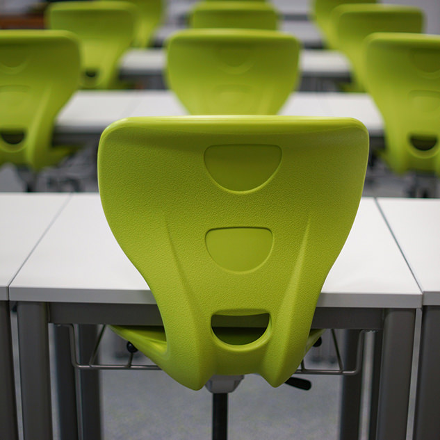 Back of bright green chair pushed in under classroom desk