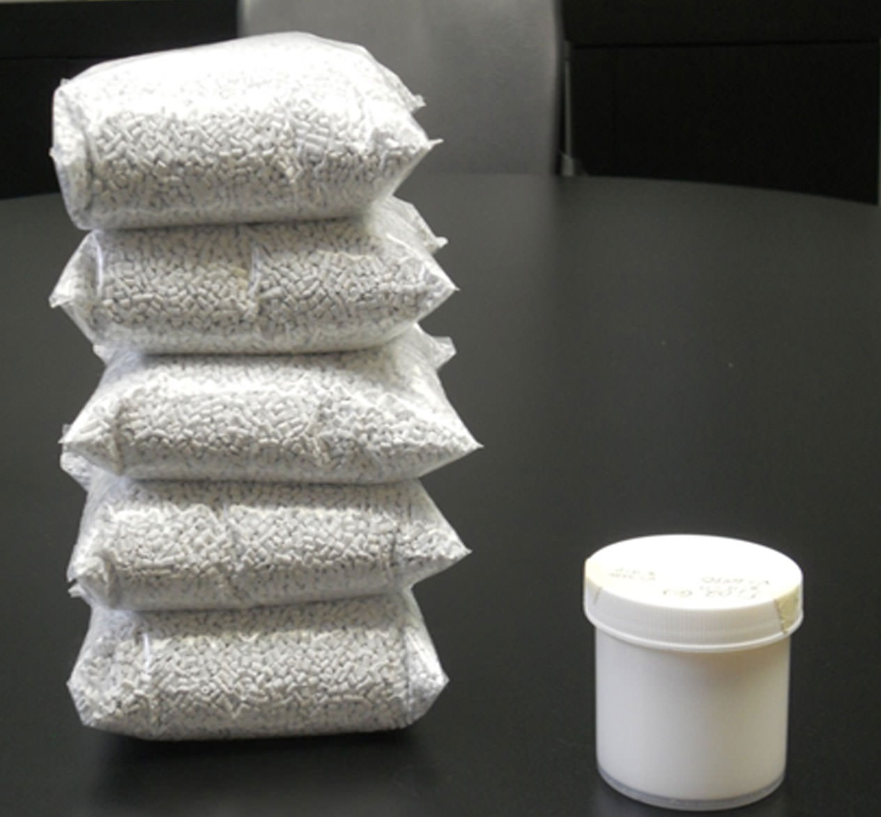 5 stacked bags of white pellet concentrates next to white container